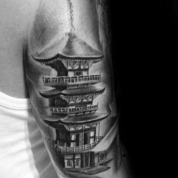 Black and grey upper arm tattoo of a detailed Japanese pagoda with realistic shading and soft light reflections for a sculpted, 3D effect.