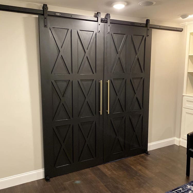 Black double sliding barn doors with a geometric X-pattern design and gold handles in a modern room.