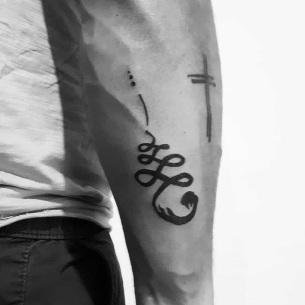 Bold Unalome tattoo on the forearm with a cross, symbolizing spiritual journey, faith, and personal growth through life’s challenges.