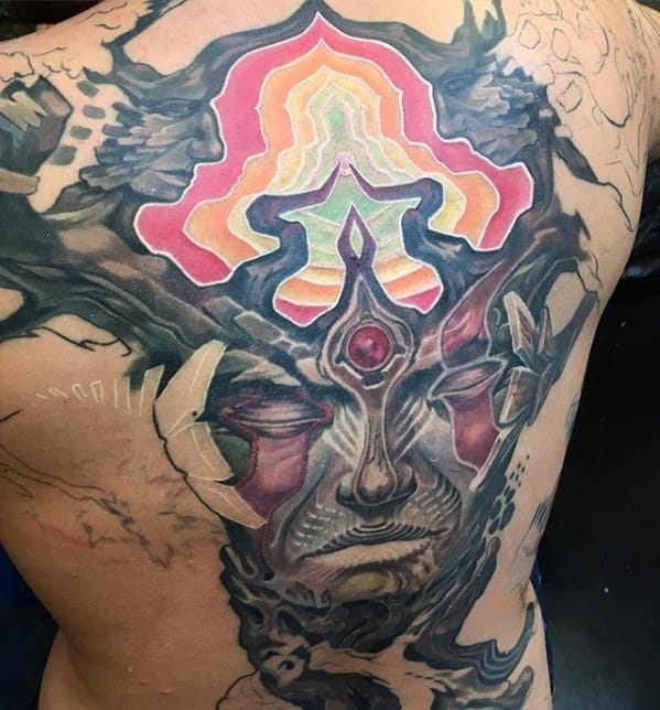 Surreal full-back tattoo of a mystical face with a third eye, abstract textures, and a vibrant psychedelic design radiating above the head.