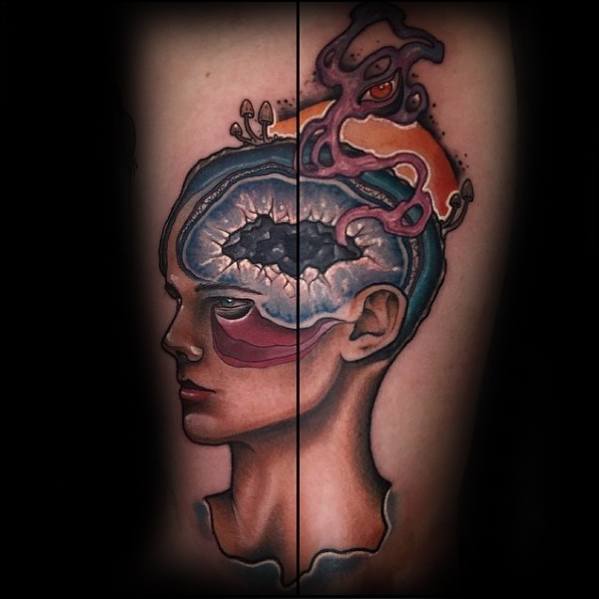Surreal tattoo of a split-faced figure with an exposed brain, cosmic and mushroom elements, and a creature emerging from the top of the head.