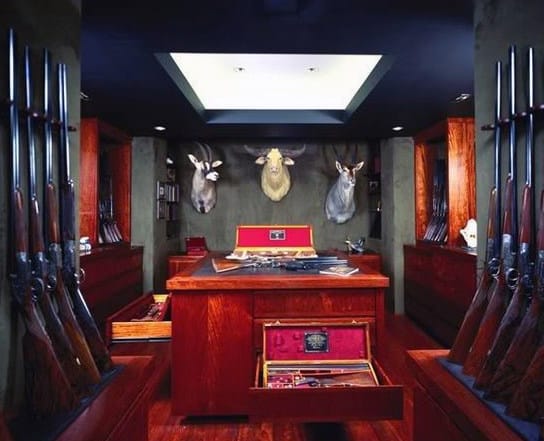 Sophisticated gun room with rich wooden cabinetry, trophy mounts, and a central island featuring secure storage drawers.