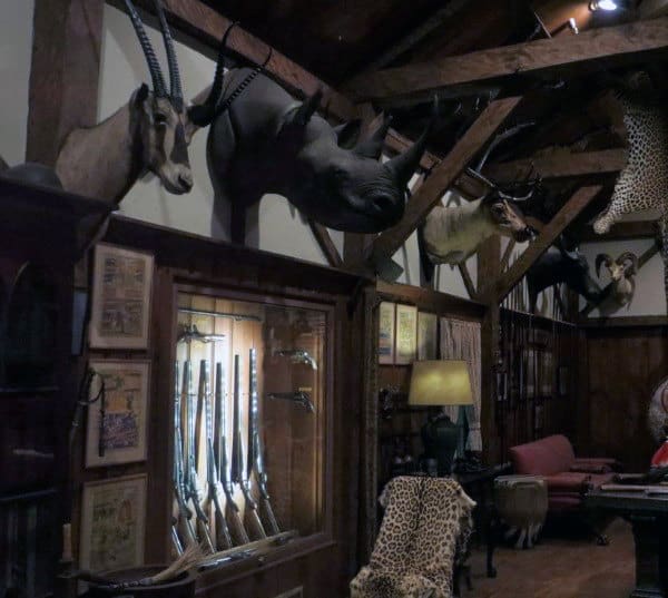 Rustic trophy room with mounted wildlife, wooden beams, and elegant gun display cases.