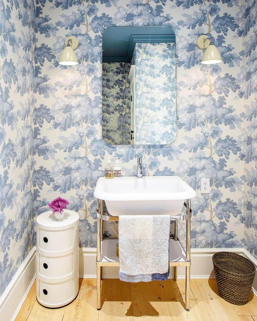 Bathroom with blue floral wallpaper, white pedestal sink, and soft lighting.