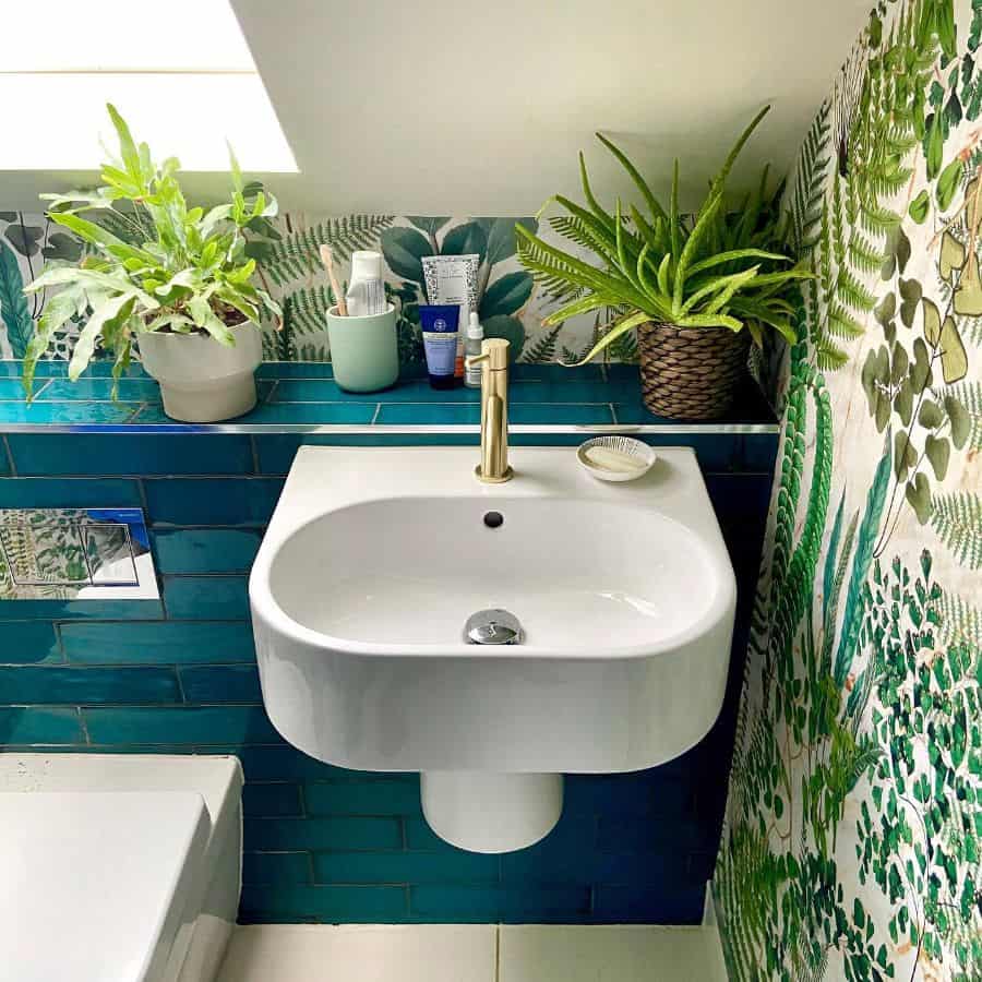 Small bathroom with green floral wallpaper, blue tiles, plants, and white sink.