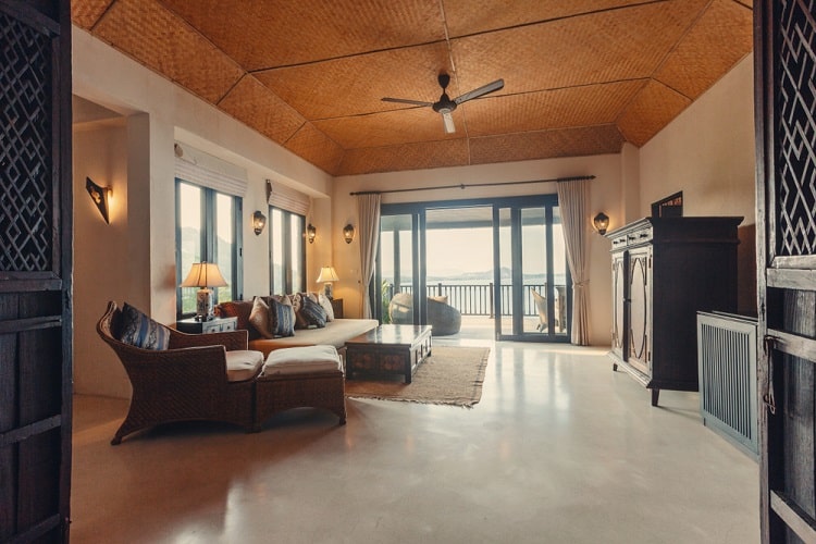 A spacious living room with wicker furniture, large windows, a vaulted ceiling, and a view of the ocean