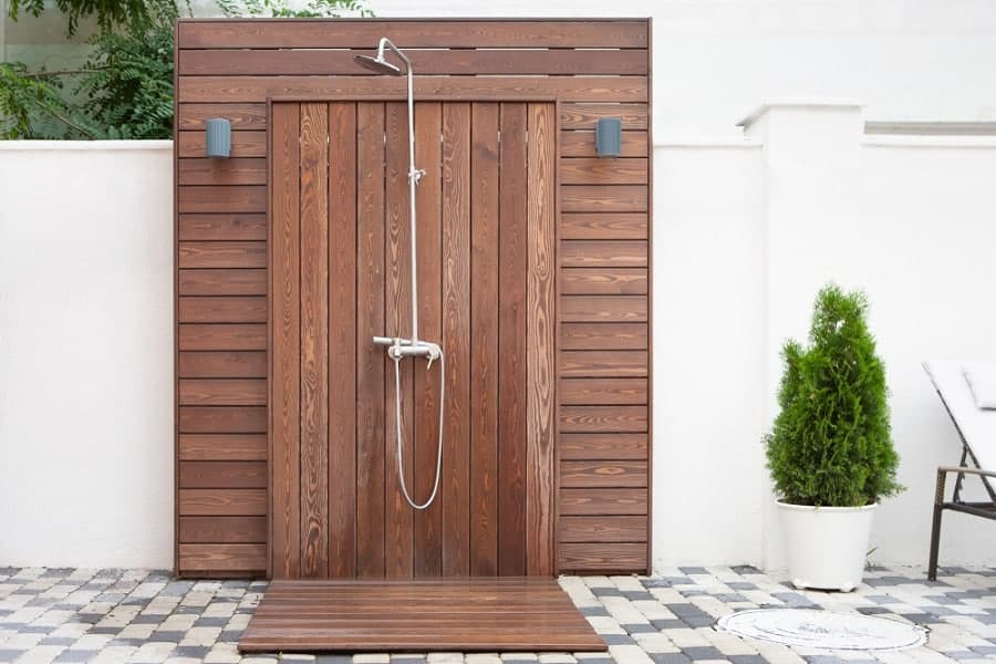 Elegant outdoor shower with rich wooden panels, minimalist chrome fixtures, and ambient wall lighting.