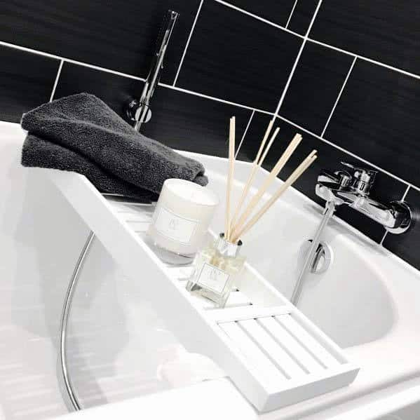 Bathtub with black tile surround, white tray, candle, reed diffuser, and folded towels.