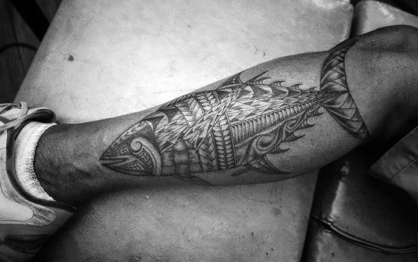 Intricate tribal-style tuna fish tattoo on a man's leg, featuring bold geometric patterns, fine line details, and strong black shading for a striking design.