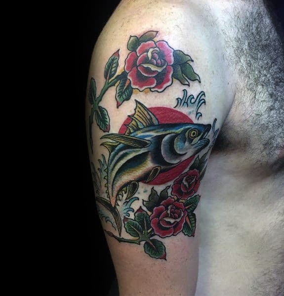 Traditional-style tuna fish tattoo on a man's upper arm, featuring bold outlines, vibrant colors, red roses, and a Japanese-inspired background.