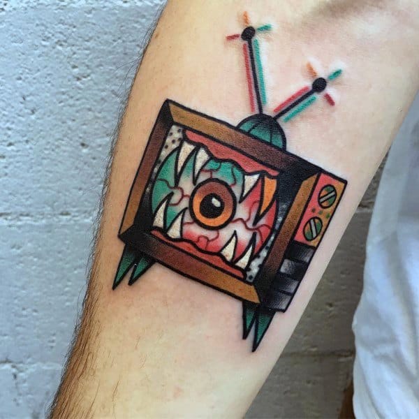 Colorful tattoo of a vintage TV with a monstrous eye and sharp teeth inside the screen, emitting electric signals from its antennas in a neo-traditional style.
