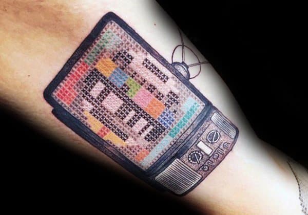 Tattoo of a vintage TV displaying a pixelated test pattern, designed with a cross-stitch effect, blending nostalgia with a unique handcrafted aesthetic.