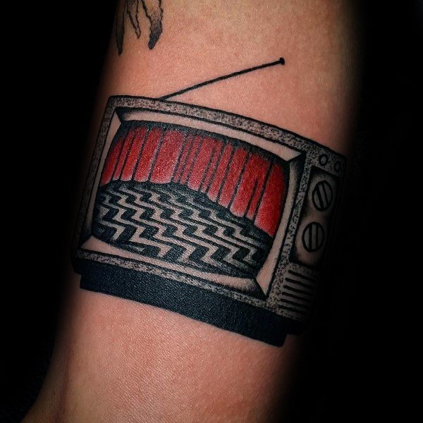 Tattoo of a vintage TV displaying a red curtain and a black-and-white zigzag floor, inspired by surreal cinema, with bold shading and classic details.