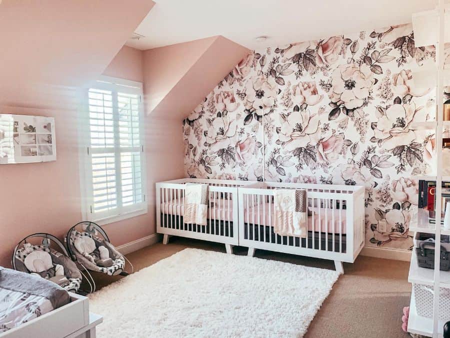 twins nursery two white cribs floral wallpaper feature wall white shelving unit white floor rug