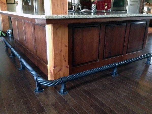 Twisted steel wire foot rail installed around a dark wood kitchen island with granite countertop on hardwood flooring.