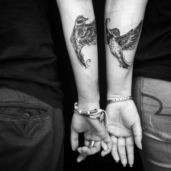 Matching forearm tattoos of birds in flight, symbolizing freedom, love, and a shared journey through life together.
