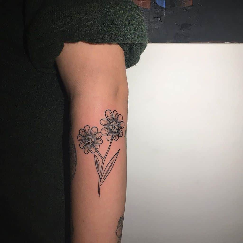 Forearm tattoo black and grey shading two daisies with eyes