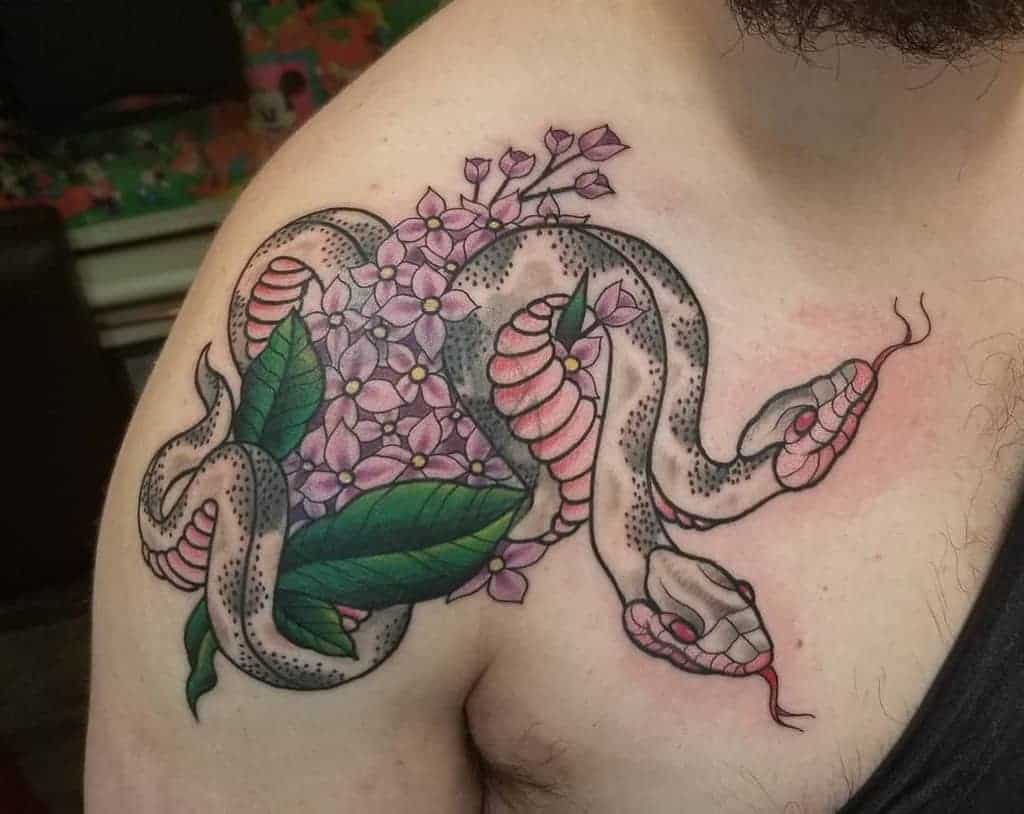 Tattoo showcases a bold two-headed snake entwined with lilac flowers, creating a unique blend of nature and mythology on the shoulder