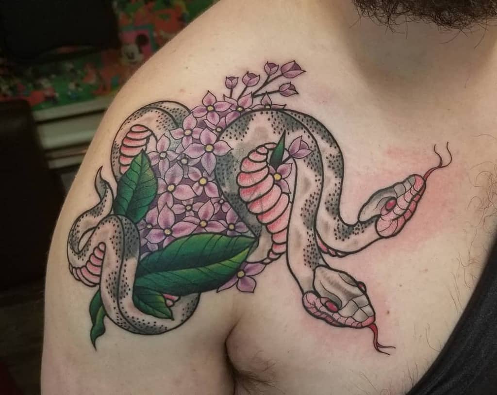 Bold neo-traditional tattoo of a coiled snake wrapped around lilac flowers and green leaves, placed on the shoulder with vibrant colors.