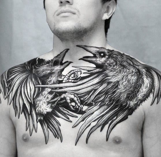 Bold black and grey chest tattoo featuring two highly detailed ravens in an intense confrontation, with intricate feather work and dynamic composition.