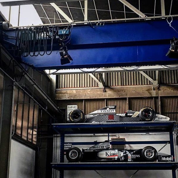 Industrial garage showcasing two levels of Formula 1 cars, perfect for motorsport enthusiasts.
