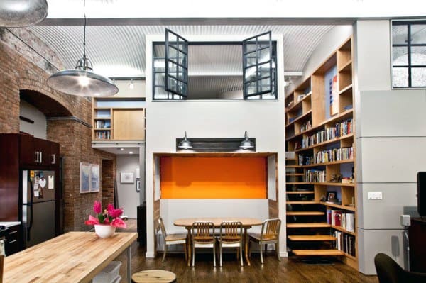 Eclectic loft with built-in bookshelves, orange accent wall, and open dining area under mezzanine.