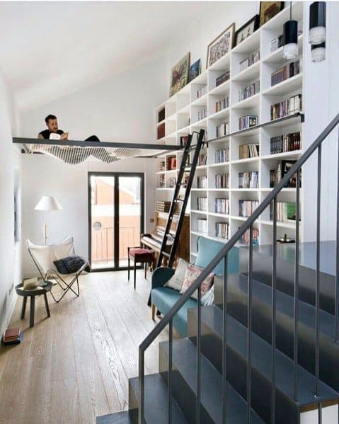 Modern loft with a bookshelf wall, ladder, net hammock, and staircase leading up