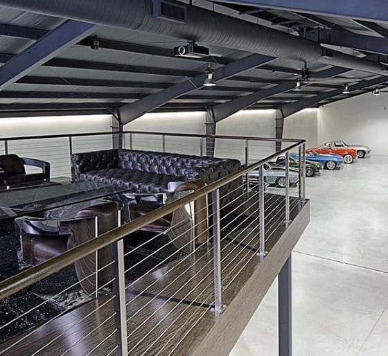 A sleek two-story garage with a lounge area overlooking a collection of classic cars.
