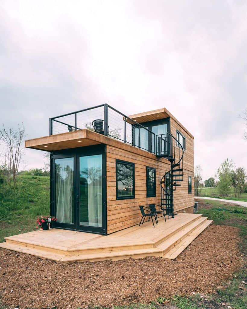 two-story shipping container home with wood plank exterior and rooftop balcony