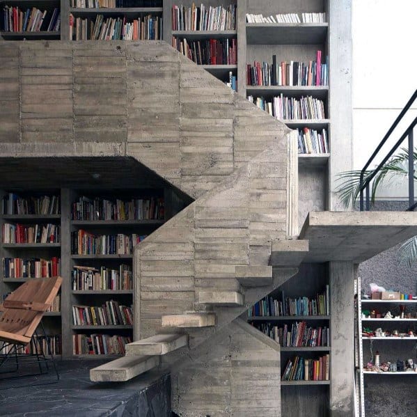 Concrete spiral staircase in a library with wooden shelves and a towering bookshelf of books