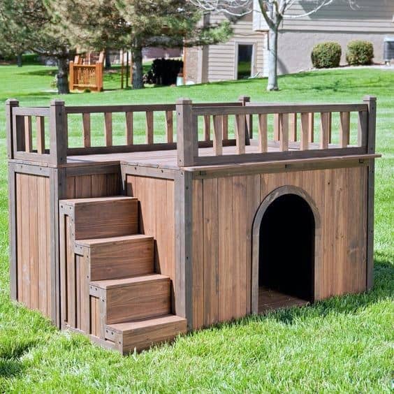 Two-story wooden dog house with stairs leading to a rooftop deck, featuring an arched entrance on the lower level, set on a grassy lawn