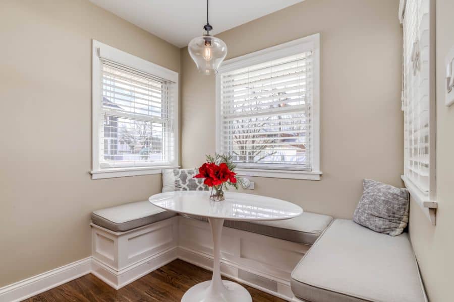 Cozy dining nook with U-shaped banquette, white round table, and red flower centerpiece.