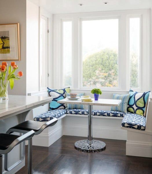 Cozy kitchen nook features a window, colorful cushions, a small table, and fresh tulips on the counter