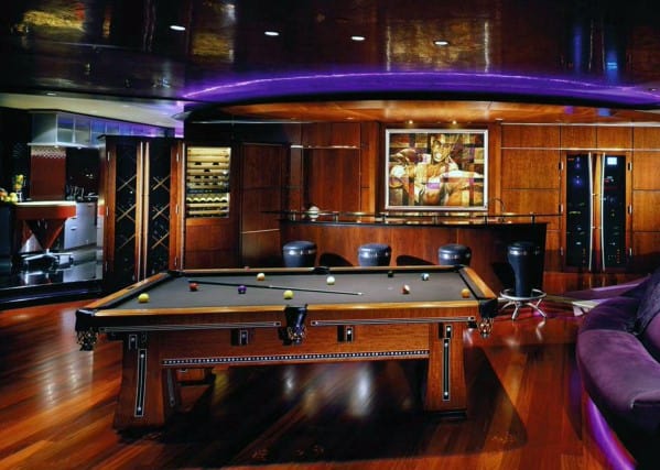 Luxurious room with a pool table, bar area, sleek wooden decor, ambient lighting, and modern art on the wall