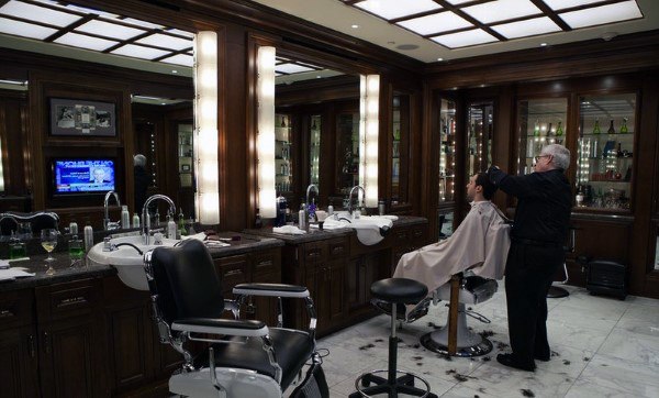 Luxury barbershop with dark wood paneling, marble floors, and illuminated mirror stations.