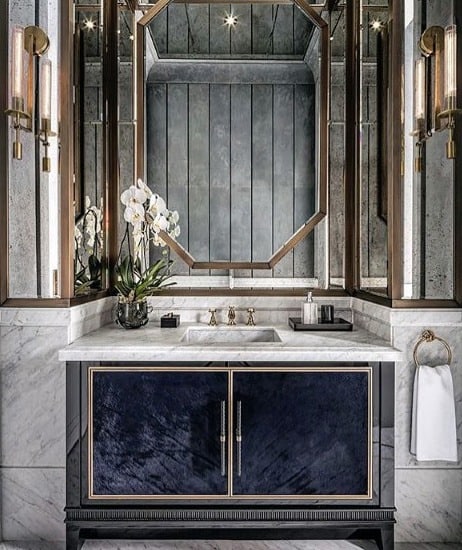 Elegant half bath with mirrored walls, marble countertop, modern lighting, and an orchid on the vanity