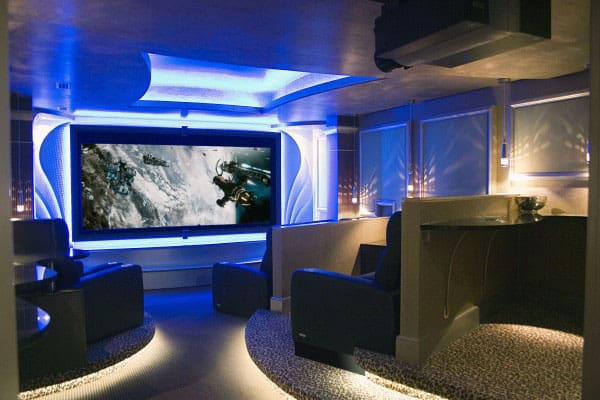 Home theater with blue lighting, large screen displaying an action scene, and luxury seating