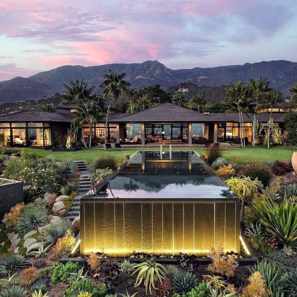 Luxury home with large pool, lush landscaping, and mountain backdrop at sunset