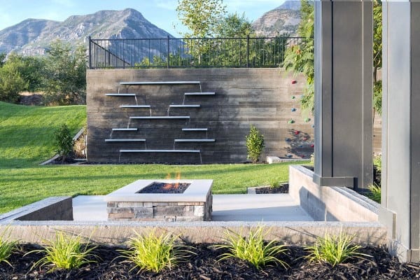 Modern backyard with slat-style wall waterfalls, fire pit, lush lawn, and mountain views.
