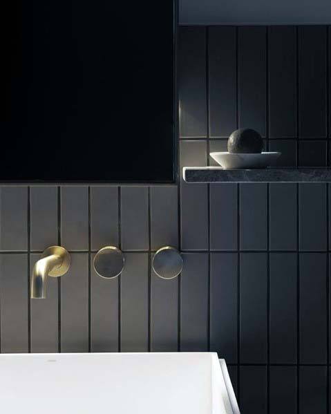 Ultra-modern black bathroom with gold faucet and sleek vertical tile design.