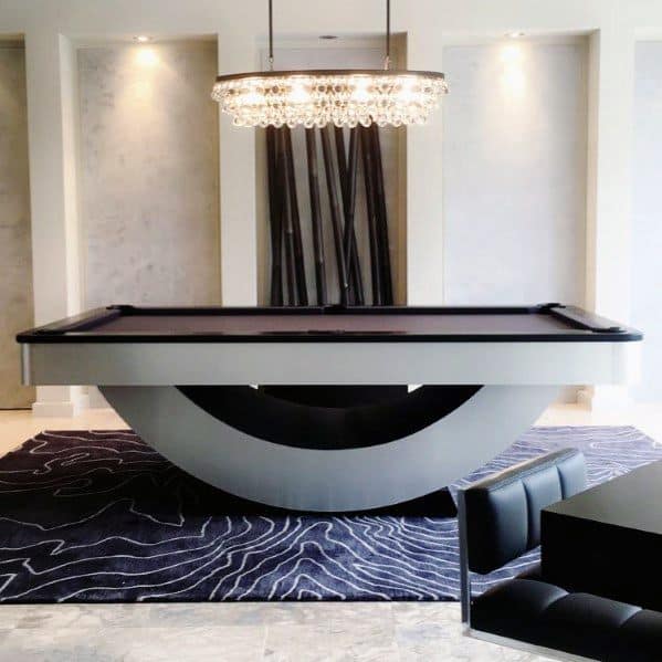 Modern billiard room with a unique curved pool table, crystal chandelier, and abstract rug design.