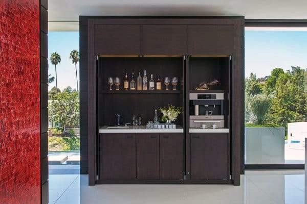 Modern coffee bar with dark cabinets, built-in coffee machine, glassware, and wine storage.