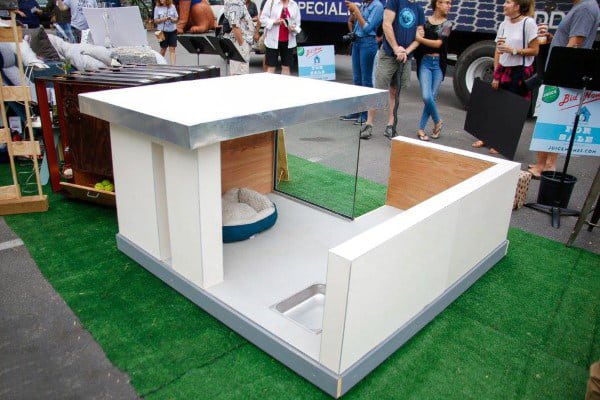Ultra-modern dog house with sleek white walls, a metal roof, and minimalist design, featuring a bed and food bowl inside, set on a grassy surface