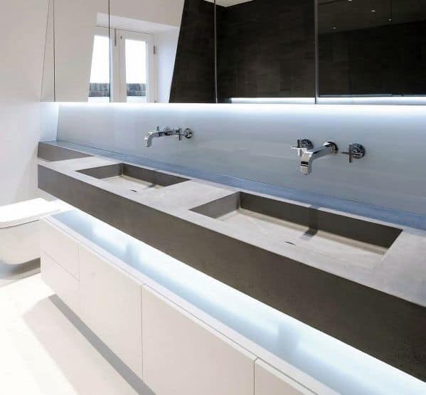 Minimalist bathroom with double concrete sinks, wall-mounted faucets, and LED backlit mirror.