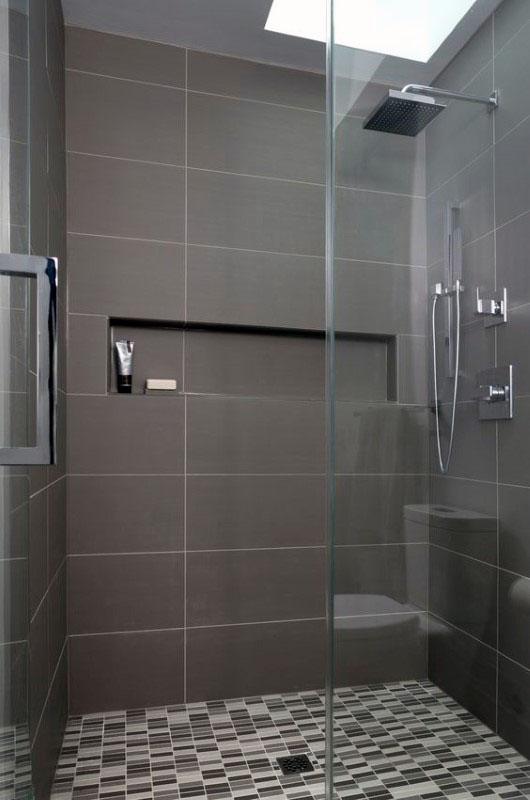 Modern shower with gray tiles, mosaic floor, recessed shelf, and glass enclosure.