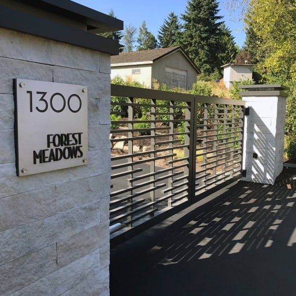 Modern metal driveway gate with horizontal slats next to a white stone pillar.