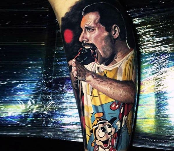 Vibrant color tattoo of Freddie Mercury passionately singing, wearing a cartoon-themed shirt with expressive stage energy and rich detailing.