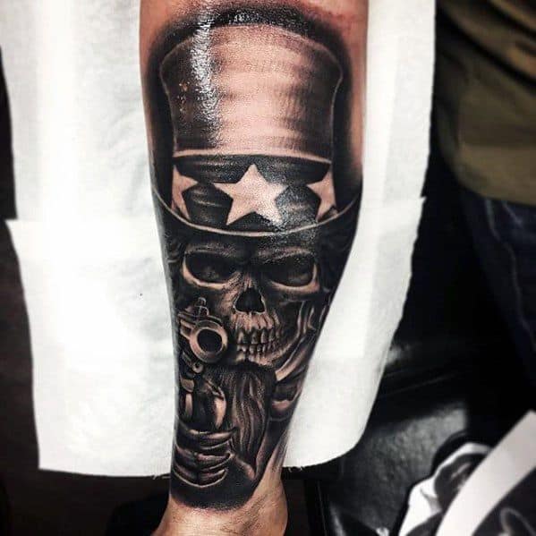 Dark and gritty Uncle Sam skull tattoo in black and gray, wearing a star-spangled hat and aiming a revolver straight ahead.