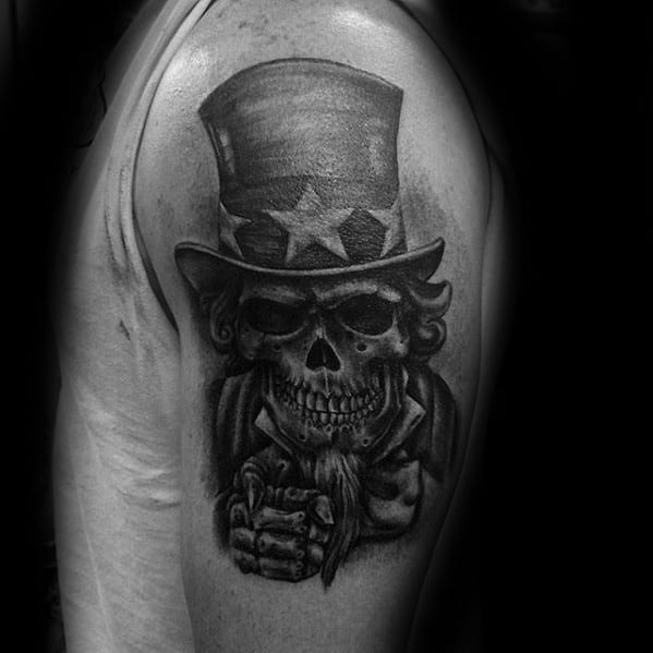 Black and gray Uncle Sam skull tattoo on the upper arm, featuring deep shadows, a sinister grin, and the iconic top hat with stars.