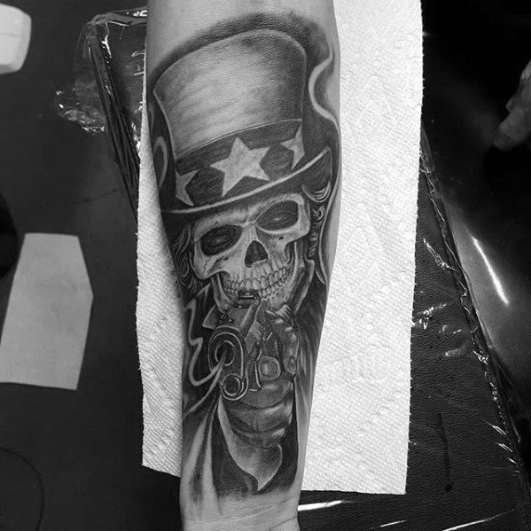 Uncle Sam skull tattoo in black and gray, with glowing eyes and a revolver pointed forward, enhanced by smoke and dramatic shading.